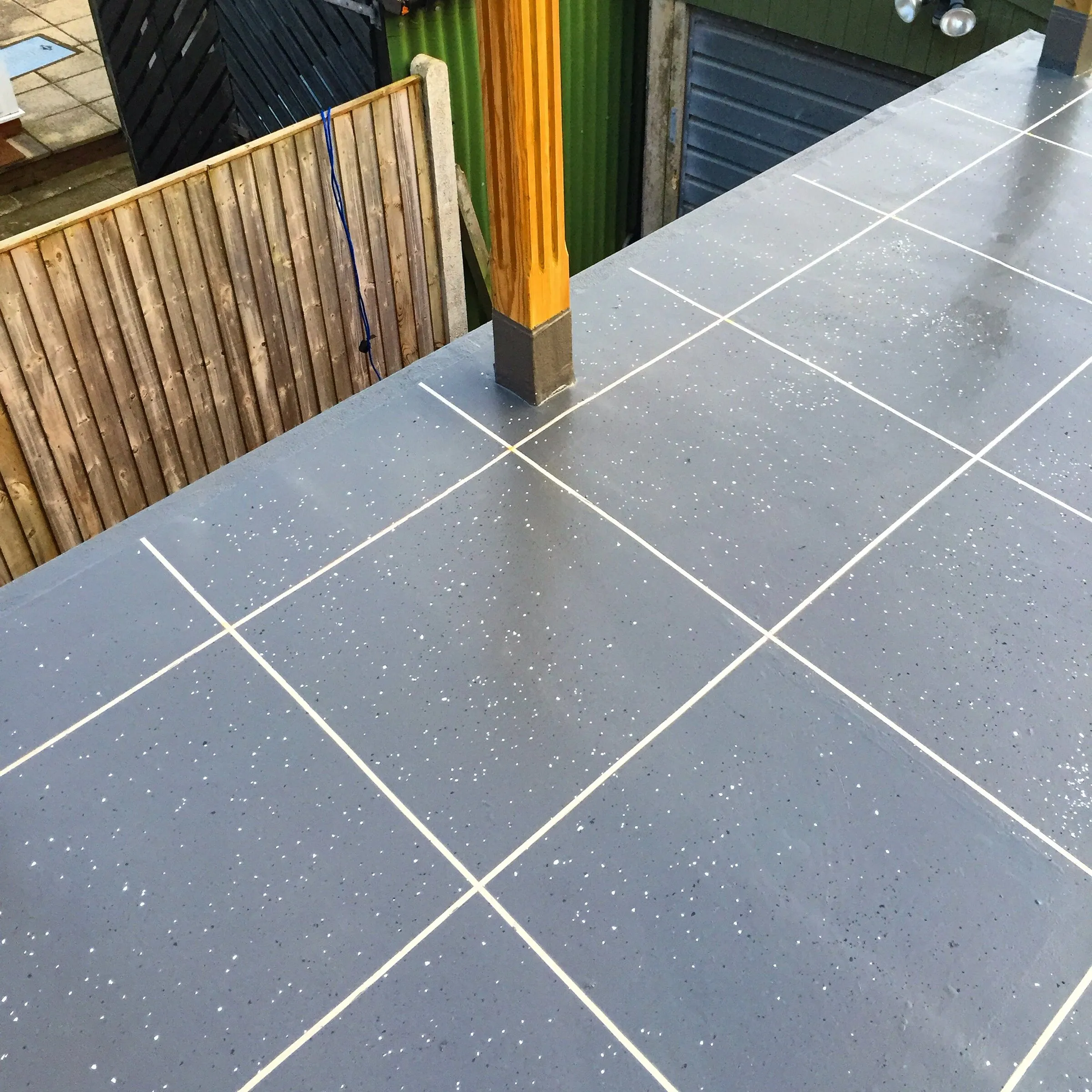 Grey tile-effect finish on a narrow terrace beside a timber fence and post