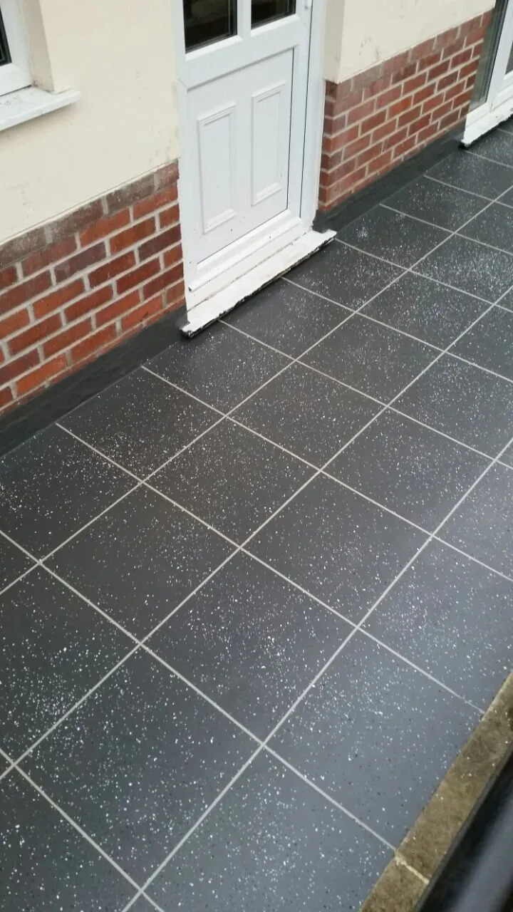 Dark grey tile-effect balcony surface running up to a white door and brick wall