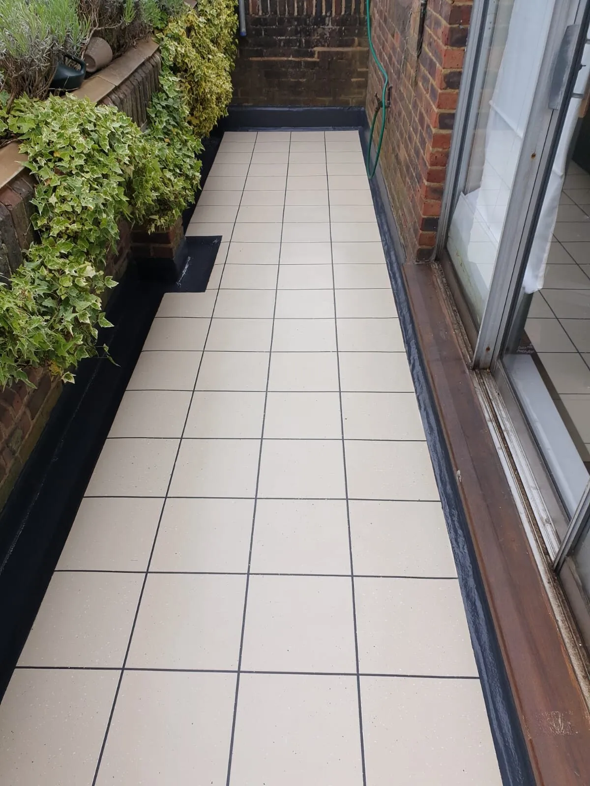Narrow balcony in a cream tile-effect finish beside sliding doors and climbing plants