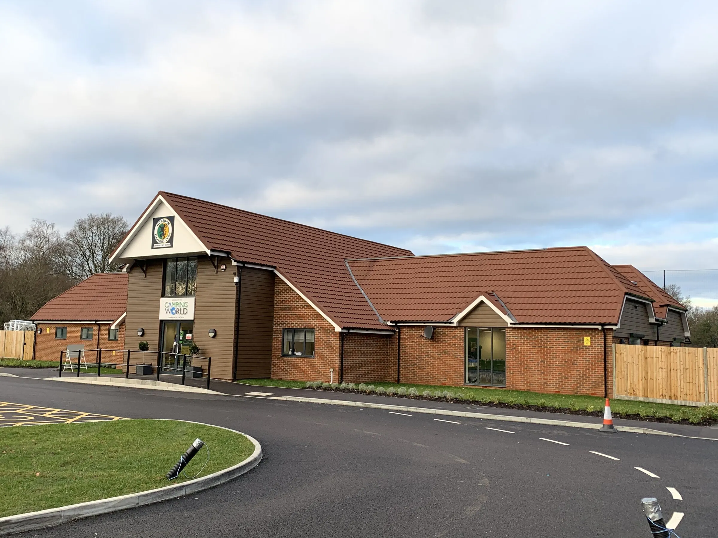 Single-storey brick building with tiled roofs and a gabled entrance, beside a new access road