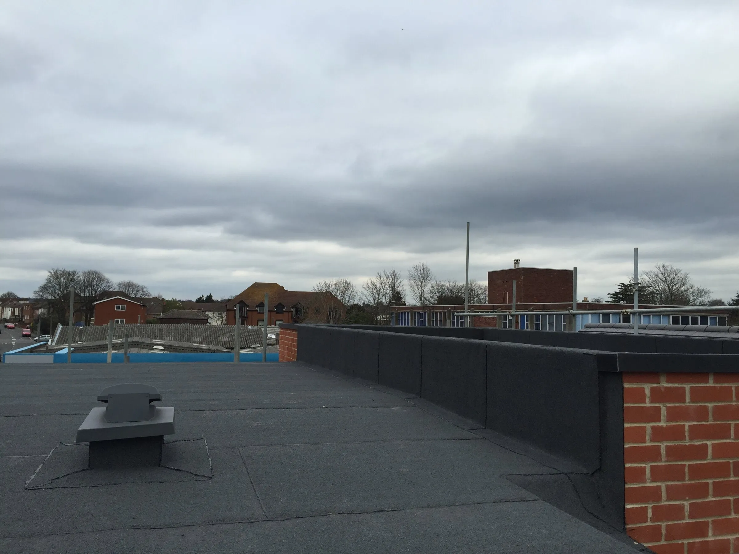 Large dark flat roof enclosed by a brick parapet under an overcast sky