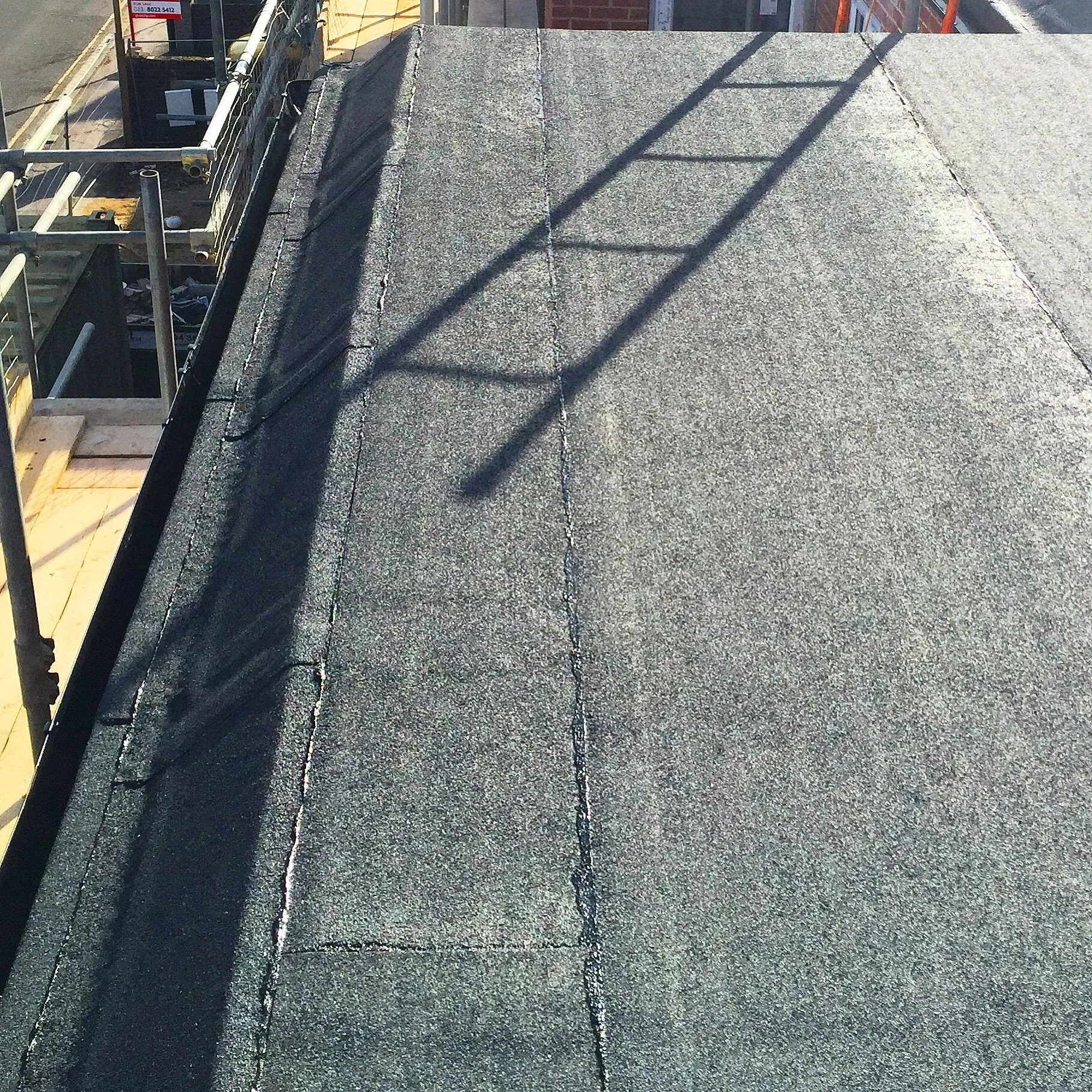 Close-up of a dark flat roof membrane running to the edge beside scaffolding