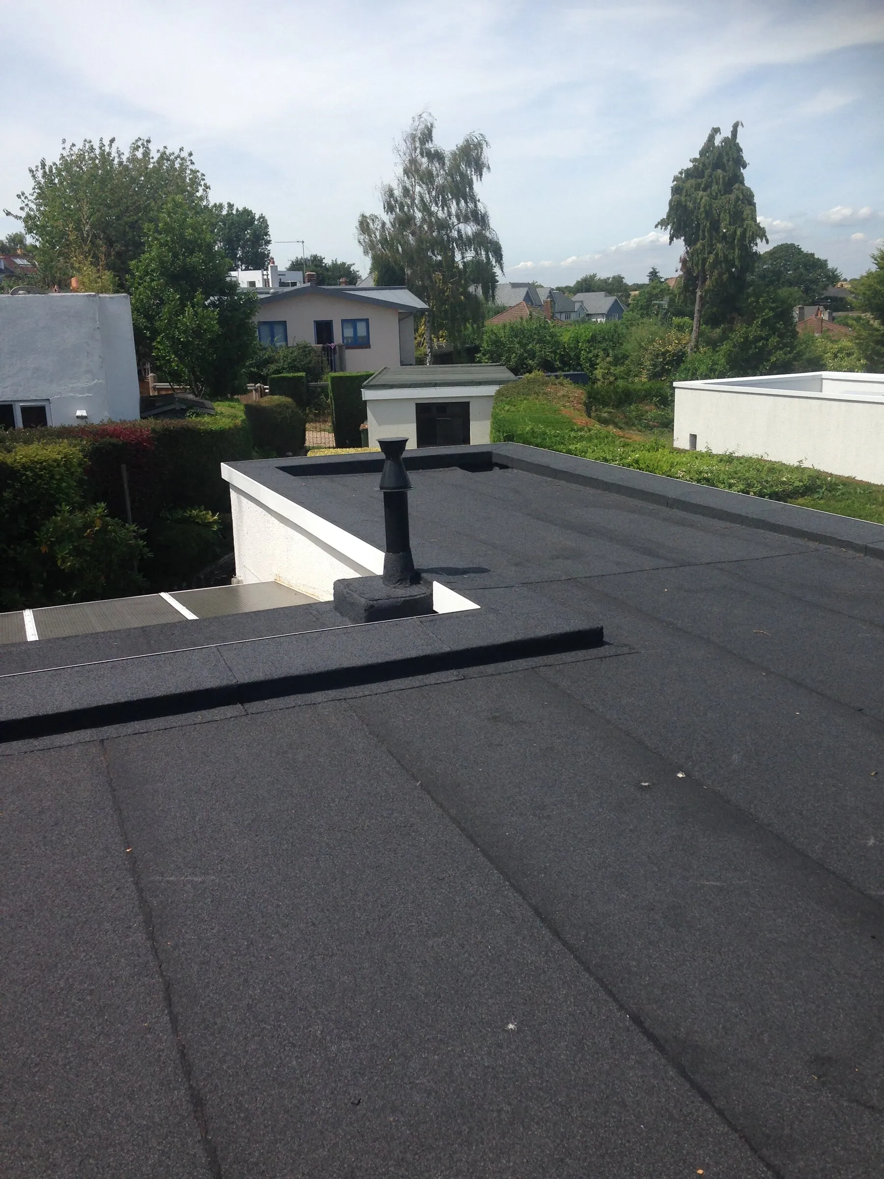 Felt flat roof with a flue pipe and white parapet, trees behind