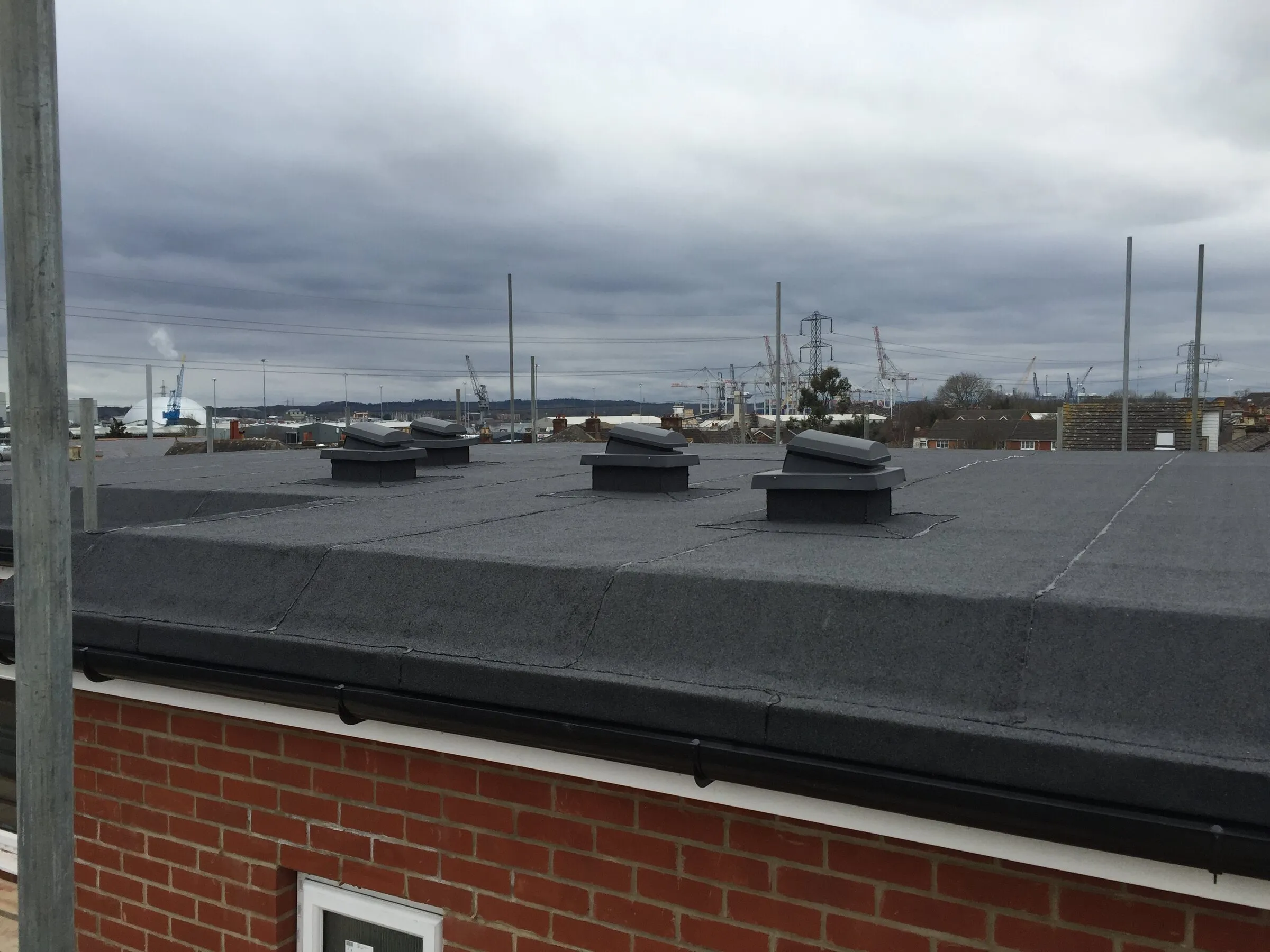Mineral felt roof with a row of vents above a brick wall