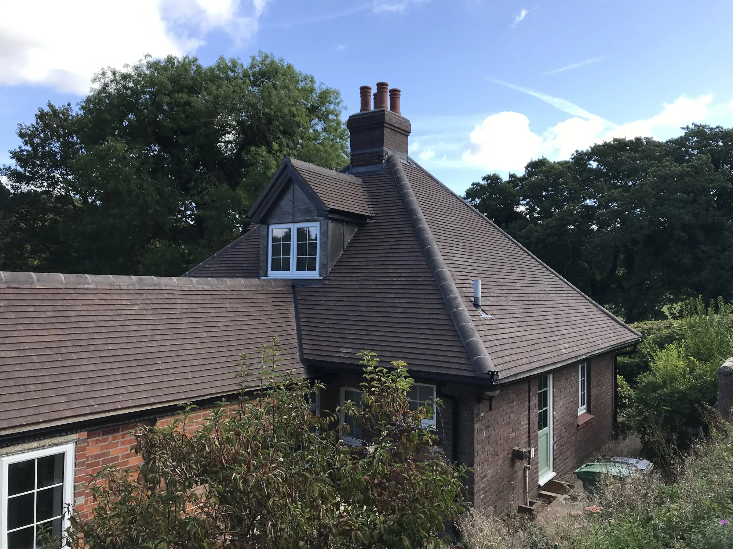 Brick cottage with a brown tiled hipped roof, dormer and central chimney