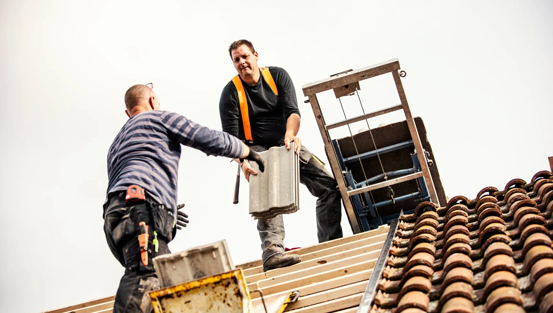 Two roofers passing roof tiles up to the ridge of a pitched roof