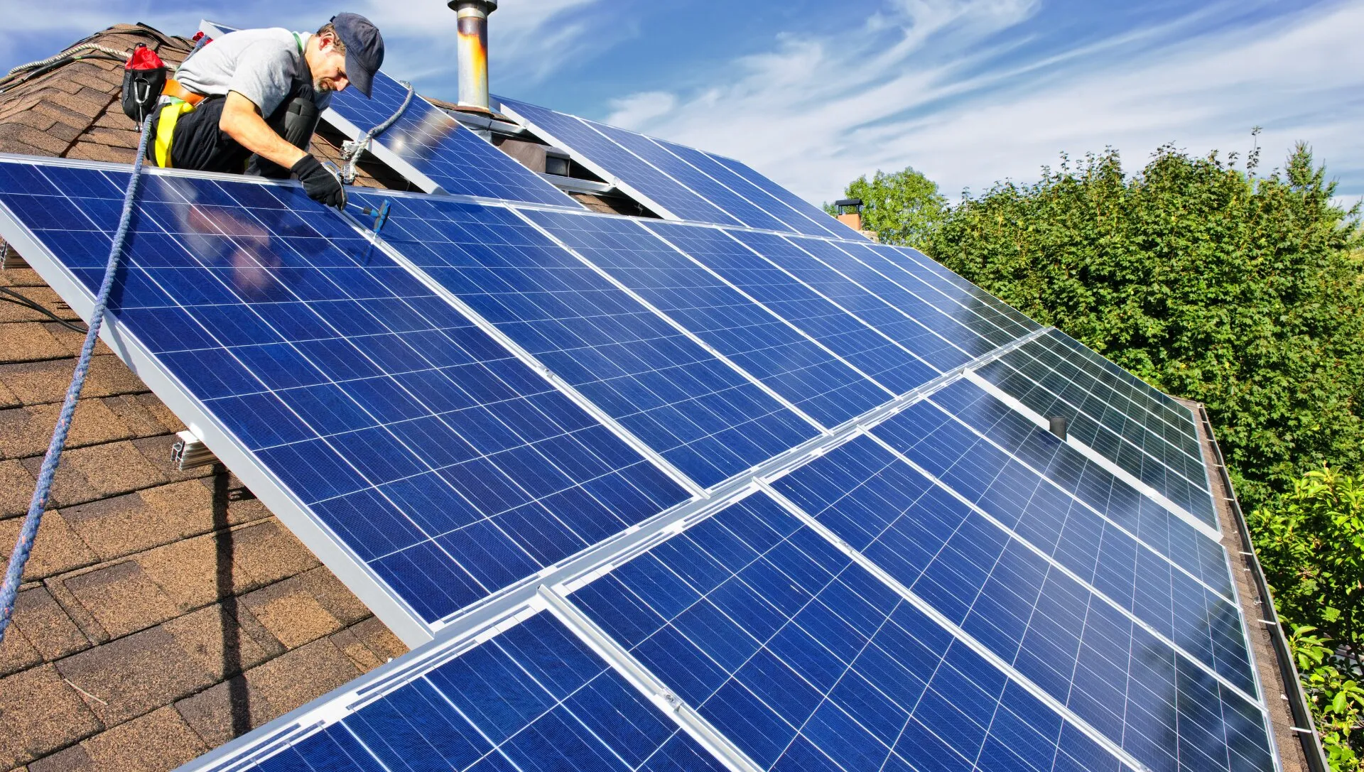 Installer fitting rows of blue solar panels on a pitched tiled roof