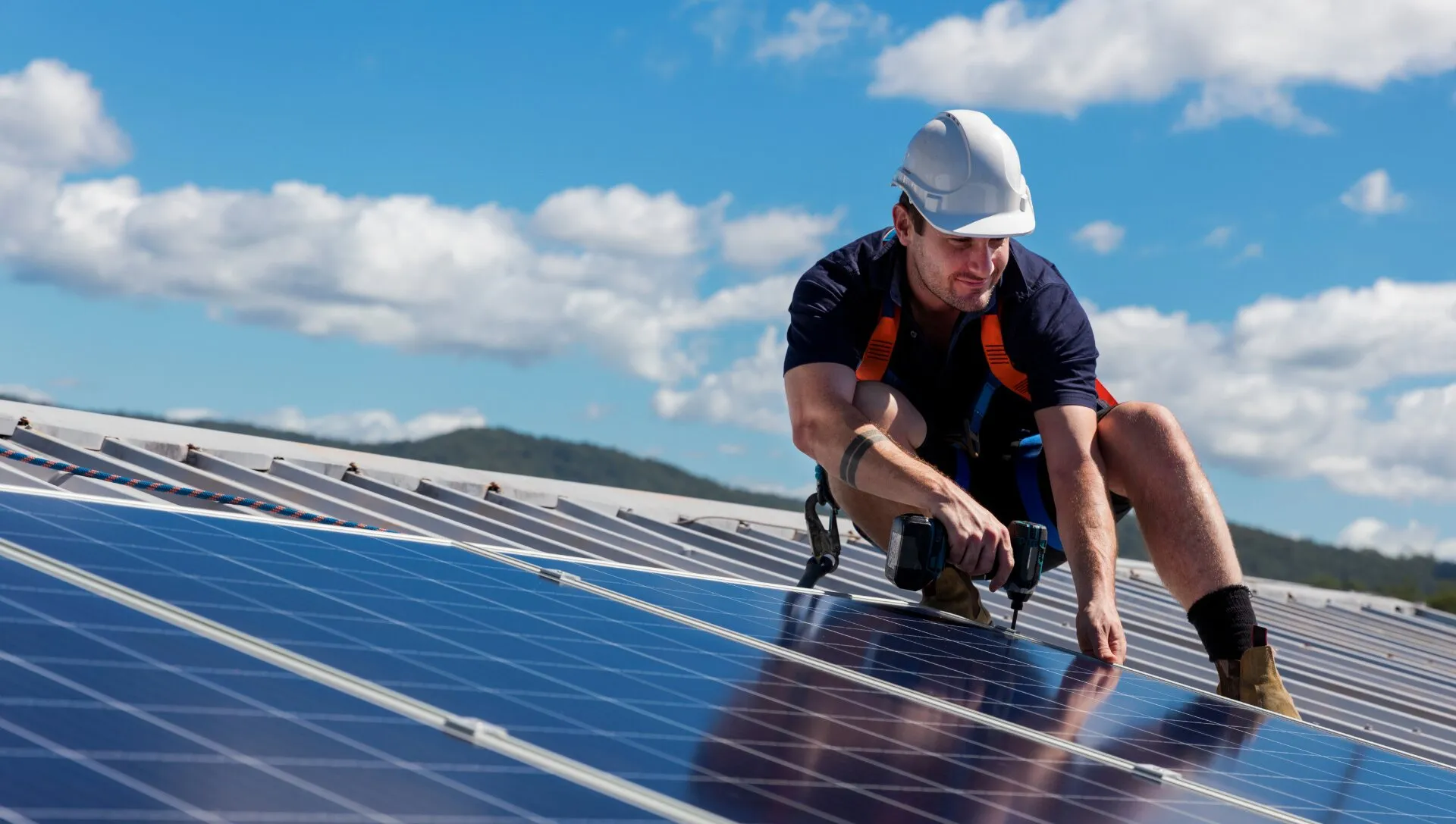 Installer in a safety harness securing solar panels on a roof under a blue sky